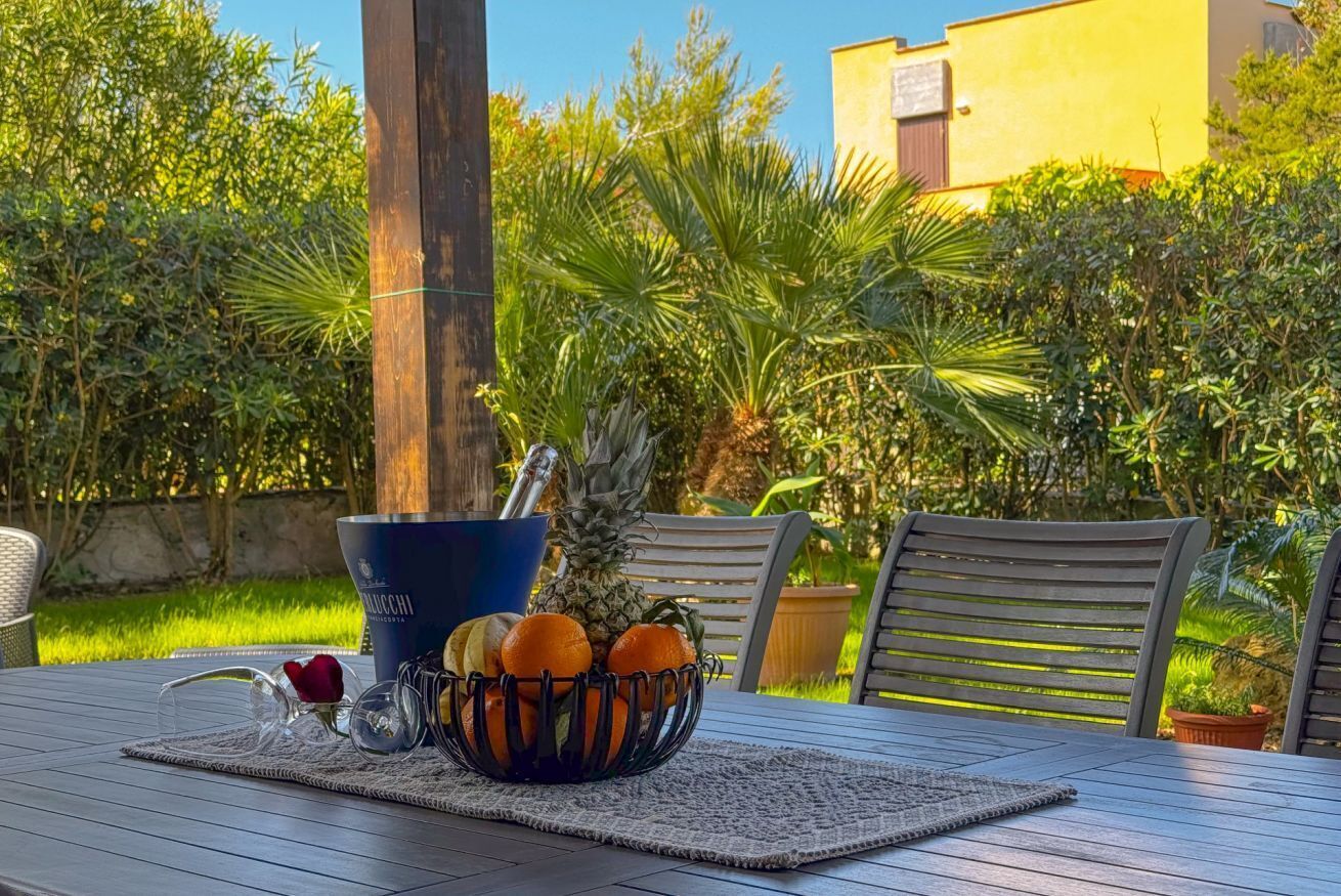A table with a fruit bowl, a bottle, and a pair of glasses.