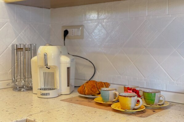 Un comptoir de cuisine avec une machine à café, un croissant et trois tasses.