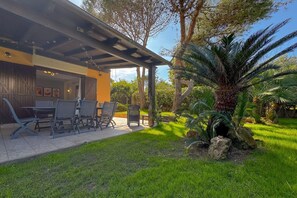 Un área de estar al aire libre cubierta con mesas y sillas, rodeada de abundante vegetación y una palmera.