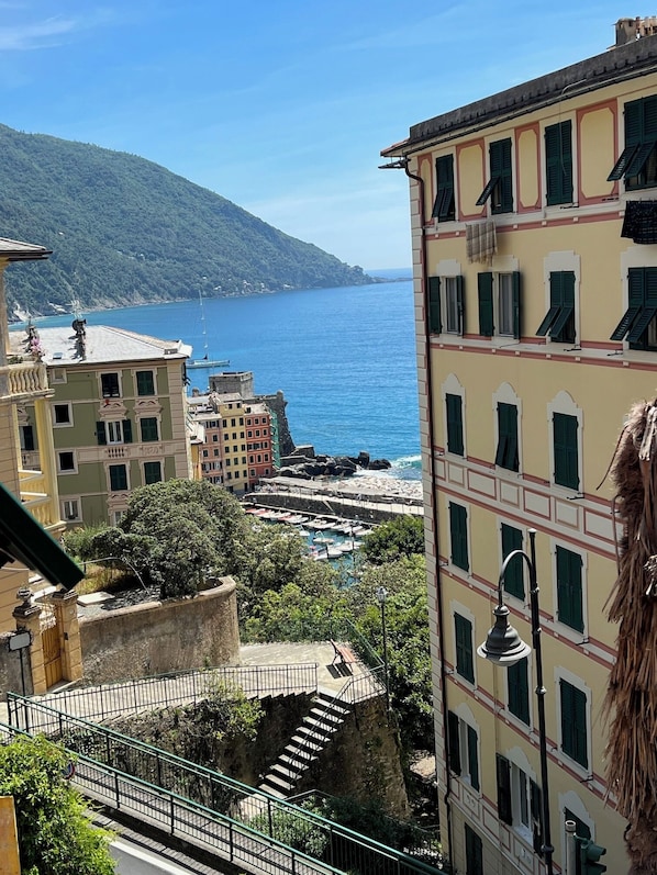 A coastal town with buildings overlooking the sea, a staircase leading down to a dock area, and a mountainous backdrop.