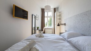 A hotel room with a large bed, a bedside table, a lamp, a window with curtains, and a wall-mounted TV. - Verde 2 - Spokojny Pok j w Dolnym Mie cie (Gdansk)