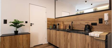 Una cocina moderna con armarios de madera, encimera negra y un espejo grande sobre el fregadero.