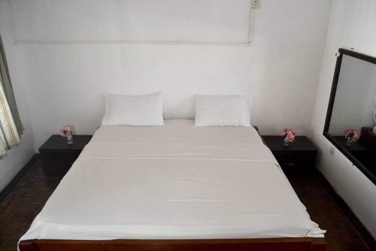 A standard hotel room with a single bed, two bedside tables, and a nightstand with a mirror.