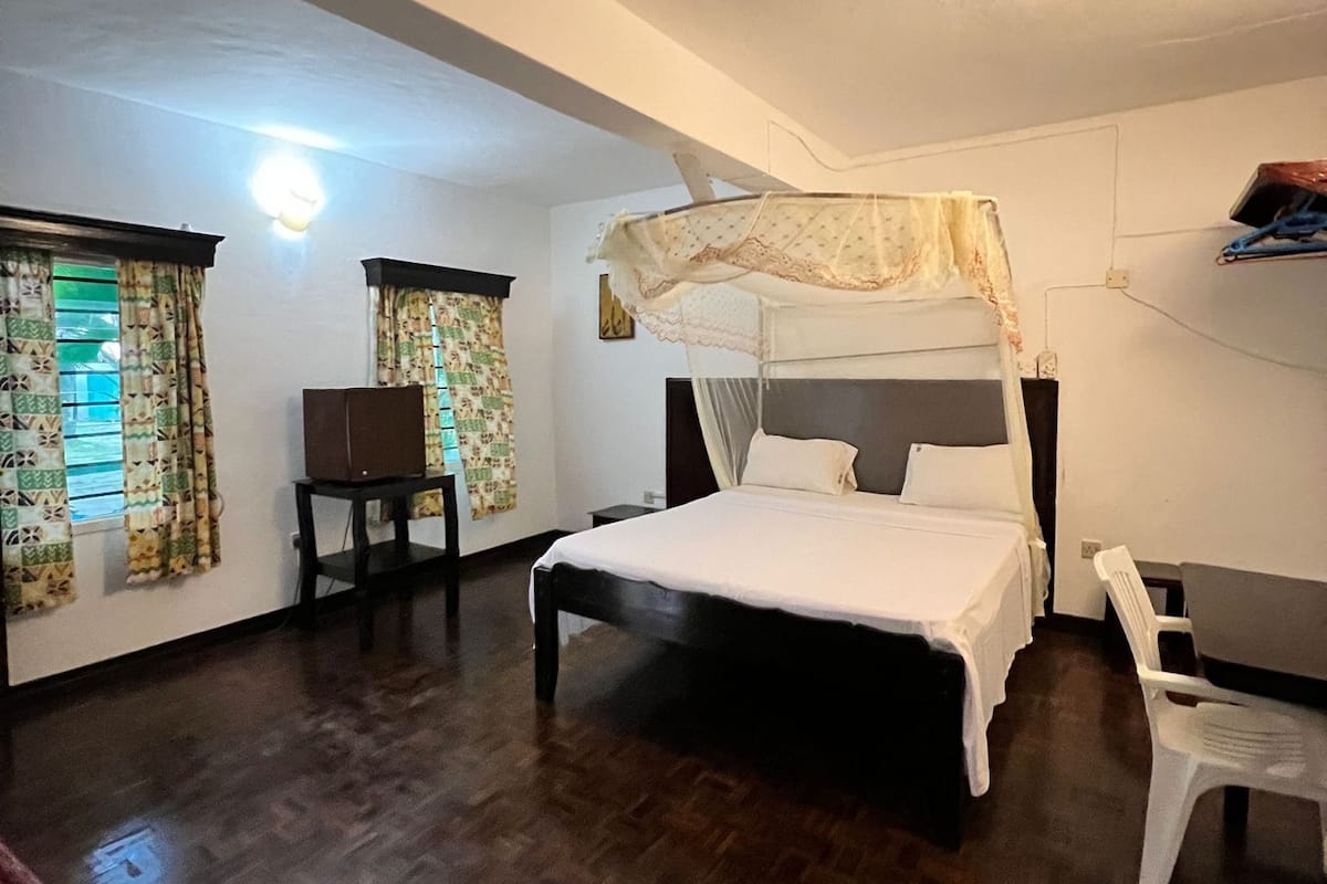 A bedroom with a four-poster bed, a desk, and a chair.