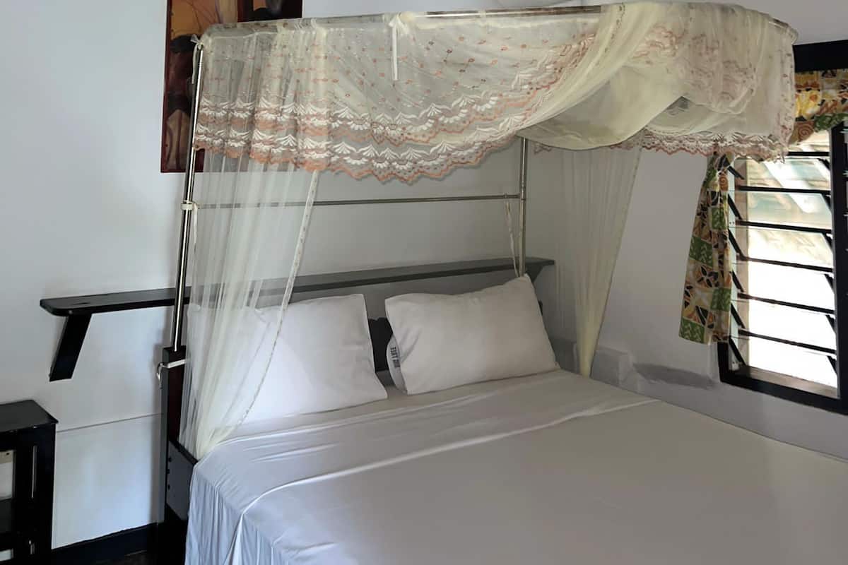 A room with a bed, a ceiling fan, a window with curtains, and a painting on the wall.