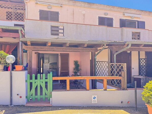 A building with a covered outdoor seating area, a green gate, and a small table with chairs.