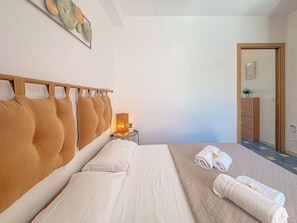 A hotel room with a large bed, a bedside table with a lamp, and a door leading to the bathroom. - Your Relaxing Spot – Nature, Comfort & Sea (Stintino)