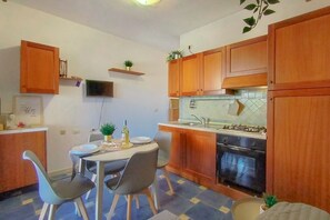 A compact kitchen with wooden cabinets, a gas stove, an oven, and a dining table with chairs.