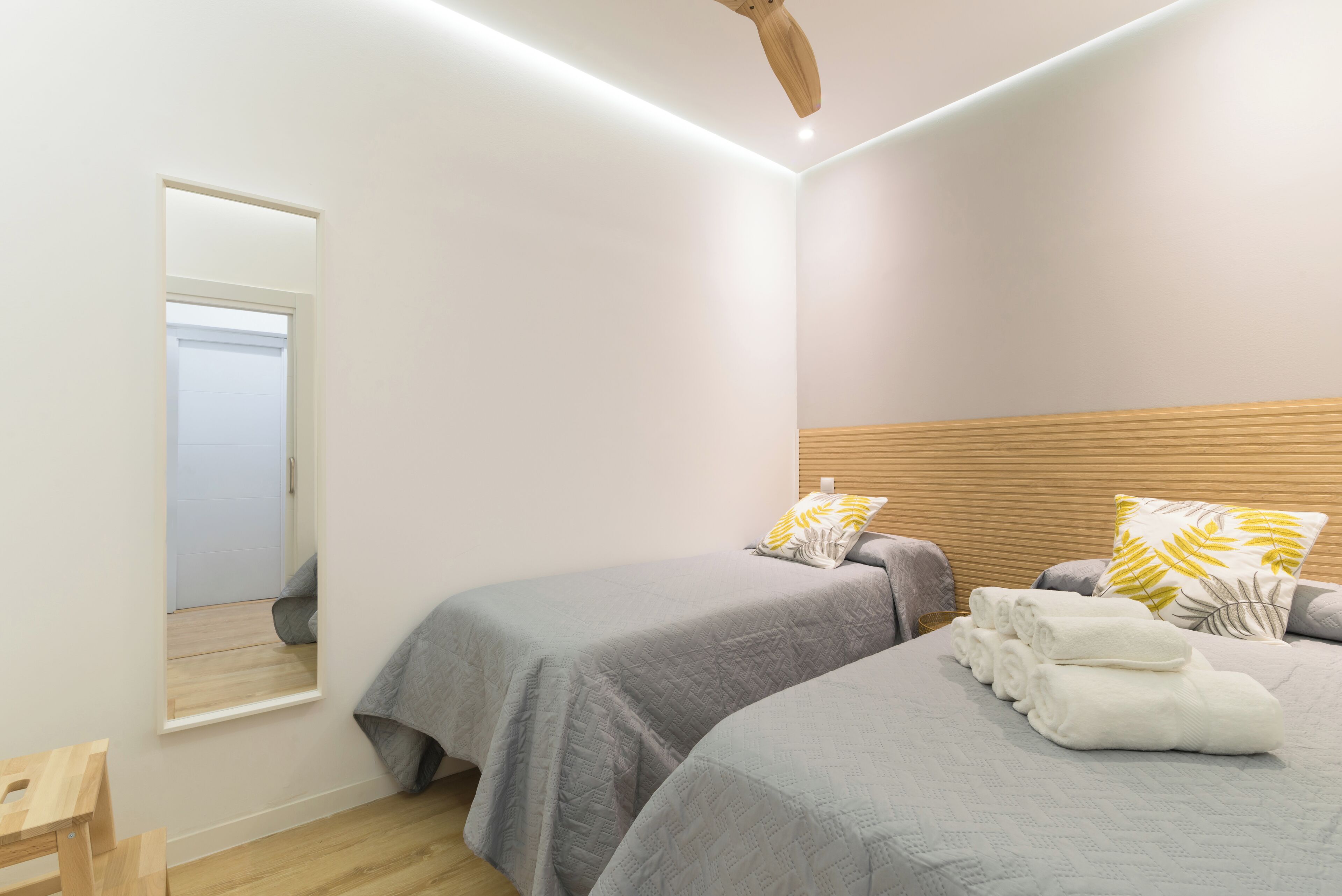 A bedroom with two beds, a wooden headboard, a mirror, and neatly folded towels.