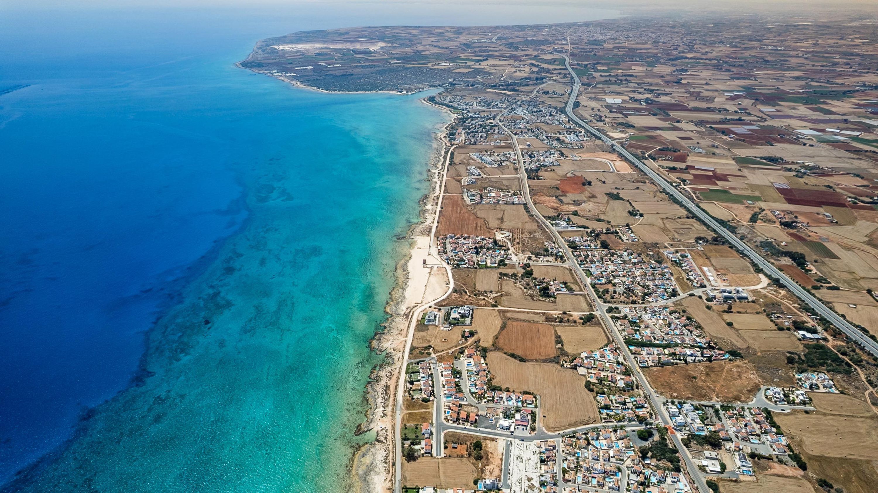 An aerial view of a coastal town with a beach, residential areas, and agricultural fields.