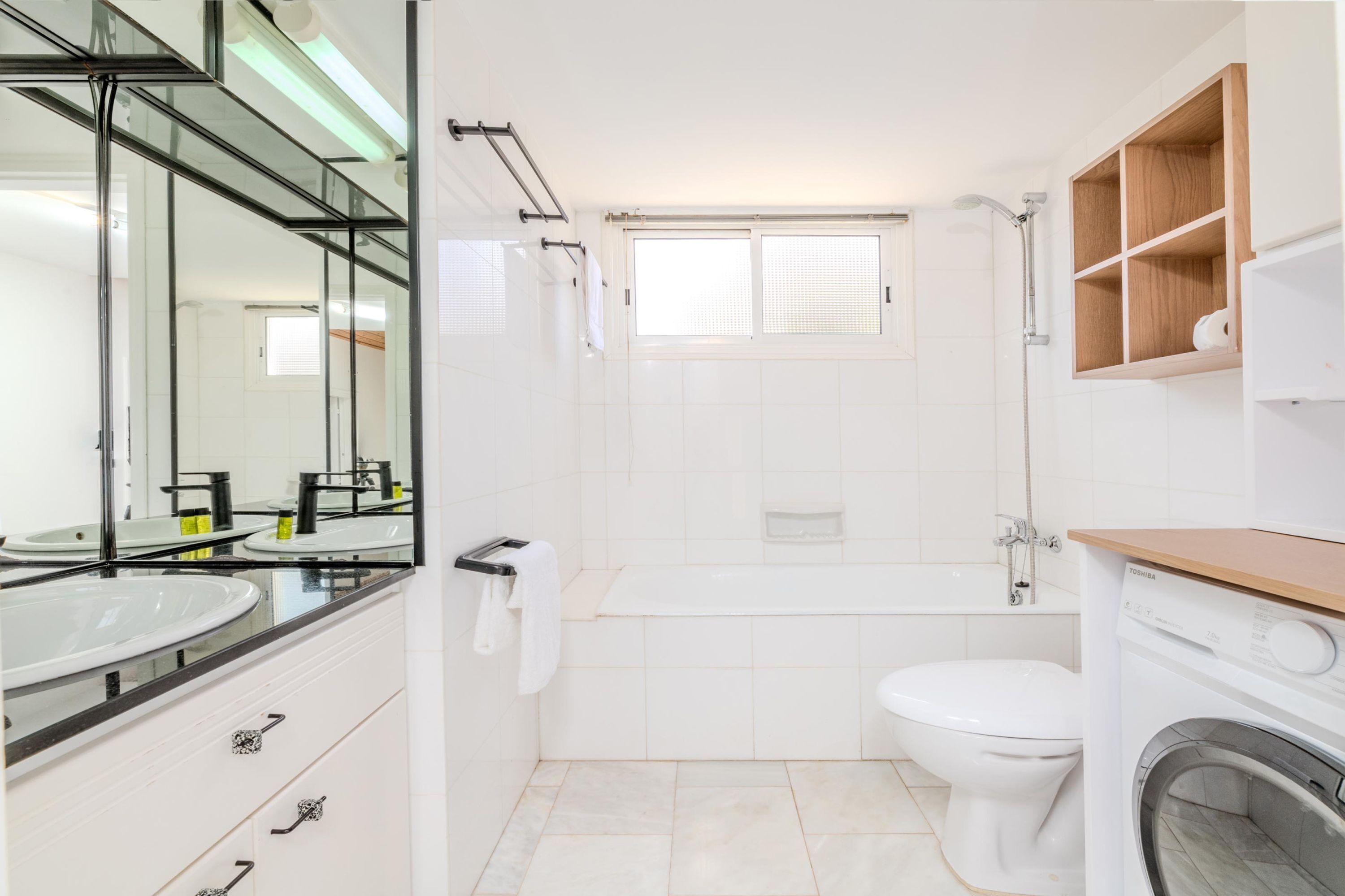 Un baño moderno con ducha de vidrio, inodoro blanco, bañera e lavadora integrada.
