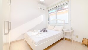 A bedroom with a bed, a nightstand, a window with a view, and an air conditioning unit. - Ayia Thekla Beach House (Sotira)
