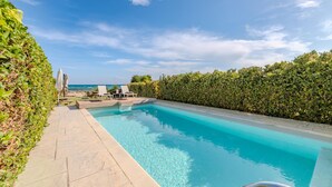 Ein rechteckiger Swimmingpool mit klarem, blauem Wasser, umgeben von einem niedrigen Heckenstreifen und einer gefliesten Liegefläche.