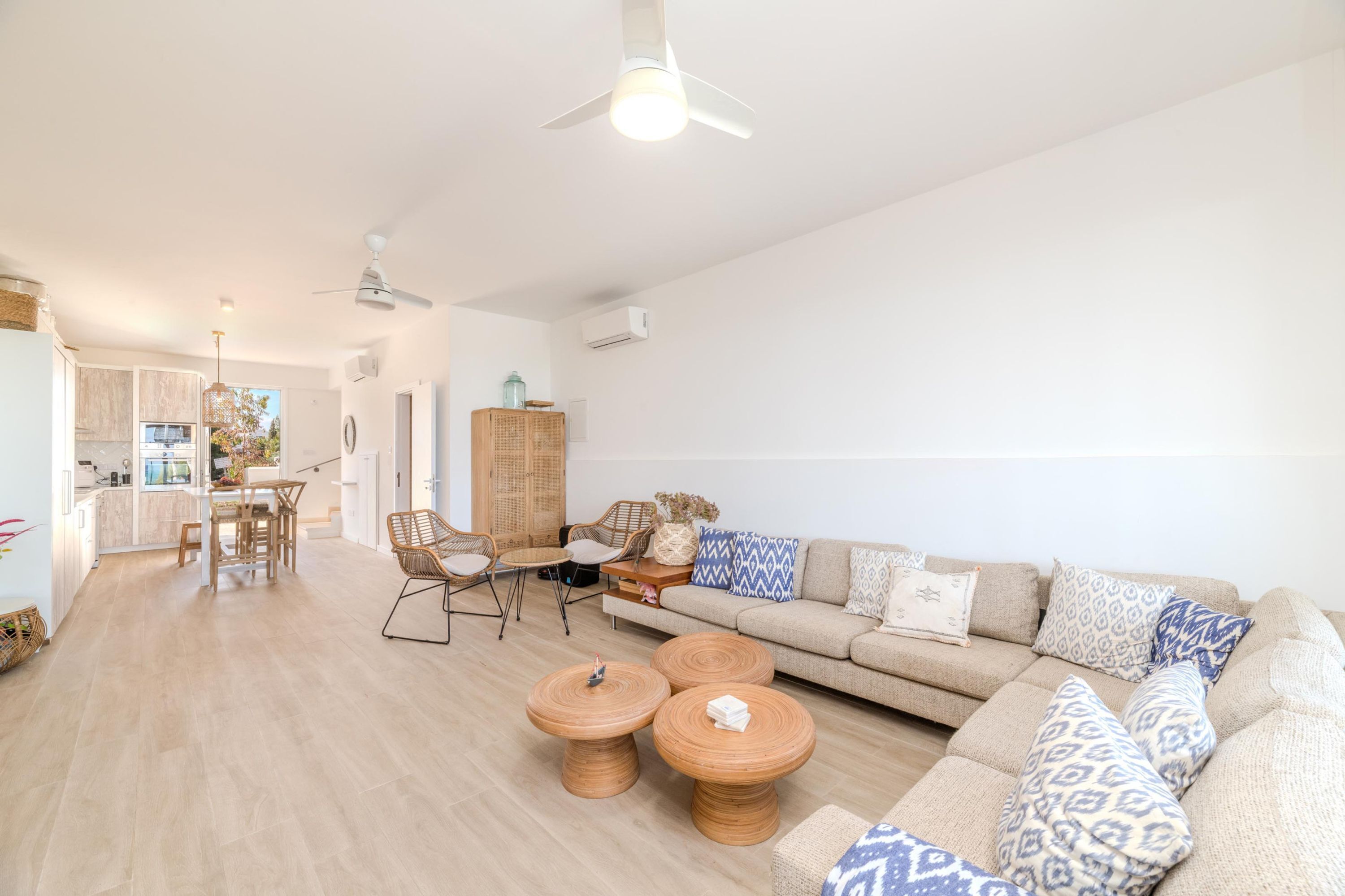 A modern living room with a sofa, two round wooden coffee tables, a dining table with chairs, and a kitchen in the background.