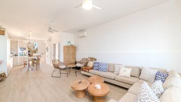 A modern living room with a sofa, two round wooden coffee tables, a dining table with chairs, and a kitchen in the background.