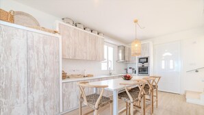 A modern kitchen with white cabinetry, a central island, and a dining area with wooden chairs. - Ayia Thekla Beach House (Sotira)