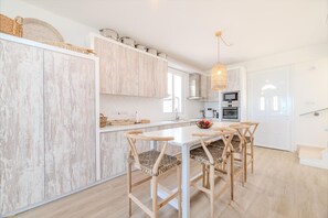 A modern kitchen with white cabinetry, a central island, and a dining area with wooden chairs.