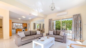 Un salon spacieux avec deux canapés, une table basse blanche et une vue sur le jardin grâce à de grandes fenêtres.