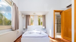 Une chambre moderne avec un grand lit, un plancher en bois, une fenêtre avec des rideaux et une porte donnant sur un espace douche.