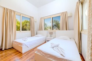 A hotel room with two single beds, a nightstand, a lamp, and large windows with curtains. - Anthorina Greco Villa 10 (Paralimni)
