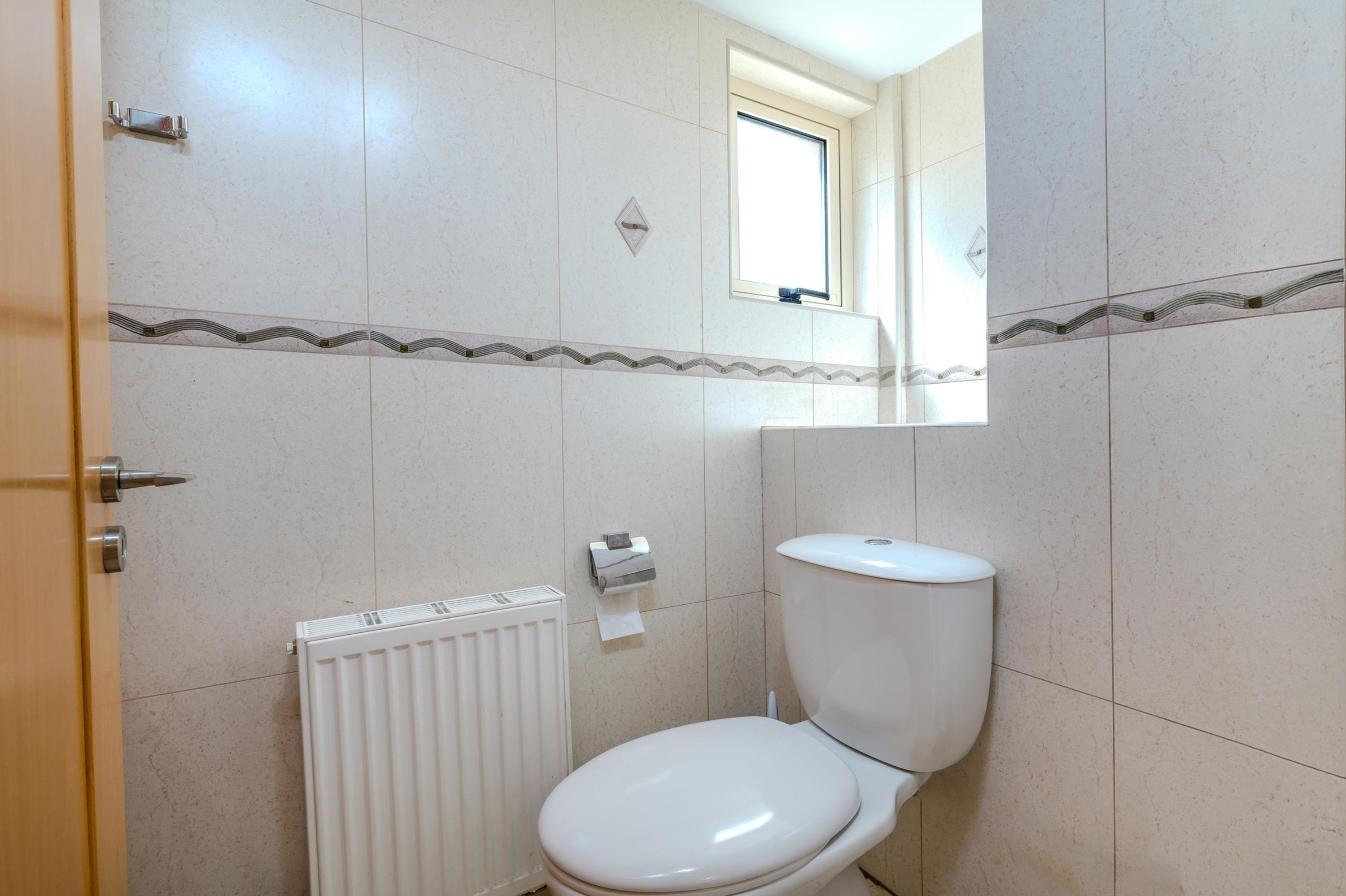 A small bathroom with a toilet, a radiator, and a window.