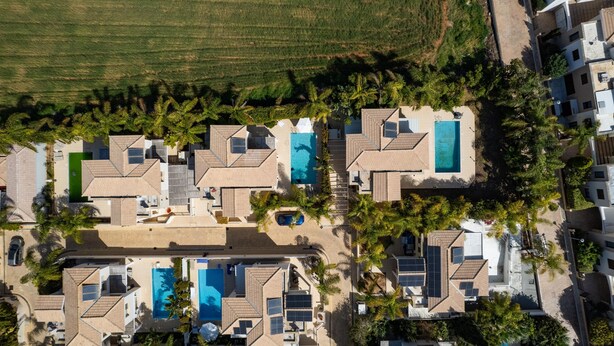 Une vue aérienne d’un quartier résidentiel composé de plusieurs maisons, chacune dotée d’une piscine et de panneaux solaires.