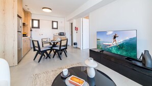 A modern living room with a large flat-screen TV, a dining area with a table and chairs, and a kitchen with wooden cabinets and appliances. - Finikoudes Marina View 102 (Larnaca)