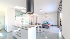 Een moderne keuken met een centraal eiland, een zithoek met een bank en televisie, en een trap naar een ander niveau.