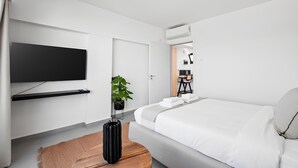 A modern hotel room with a large bed, a flat-screen TV mounted on the wall, a potted plant, and a wooden side table. - Finikoudes Marina View 202 (Larnaca)