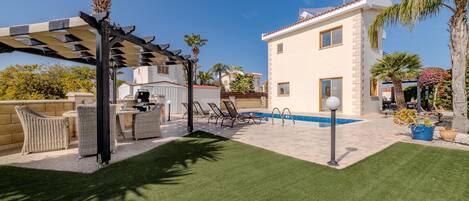 A backyard with a pool, outdoor furniture, and a pergola.