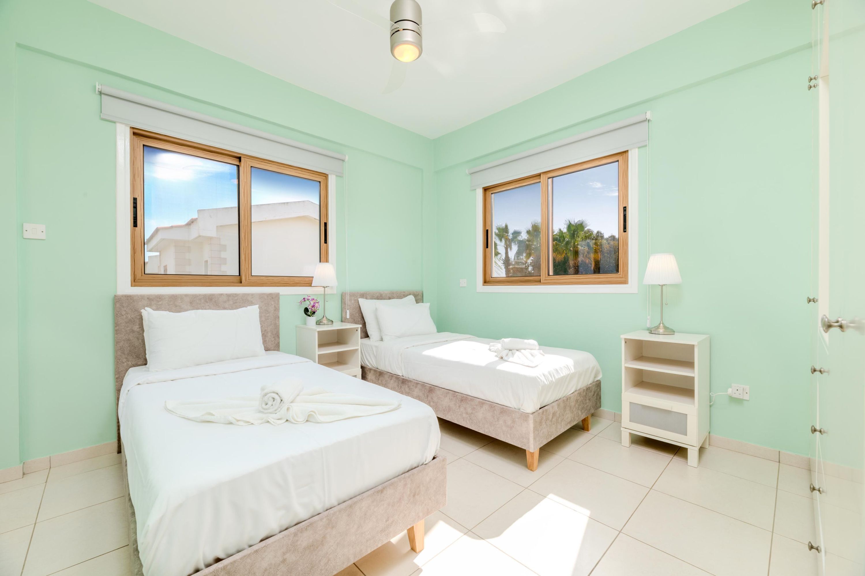 A room with two beds, a window with a view, and a bedside table with a lamp.