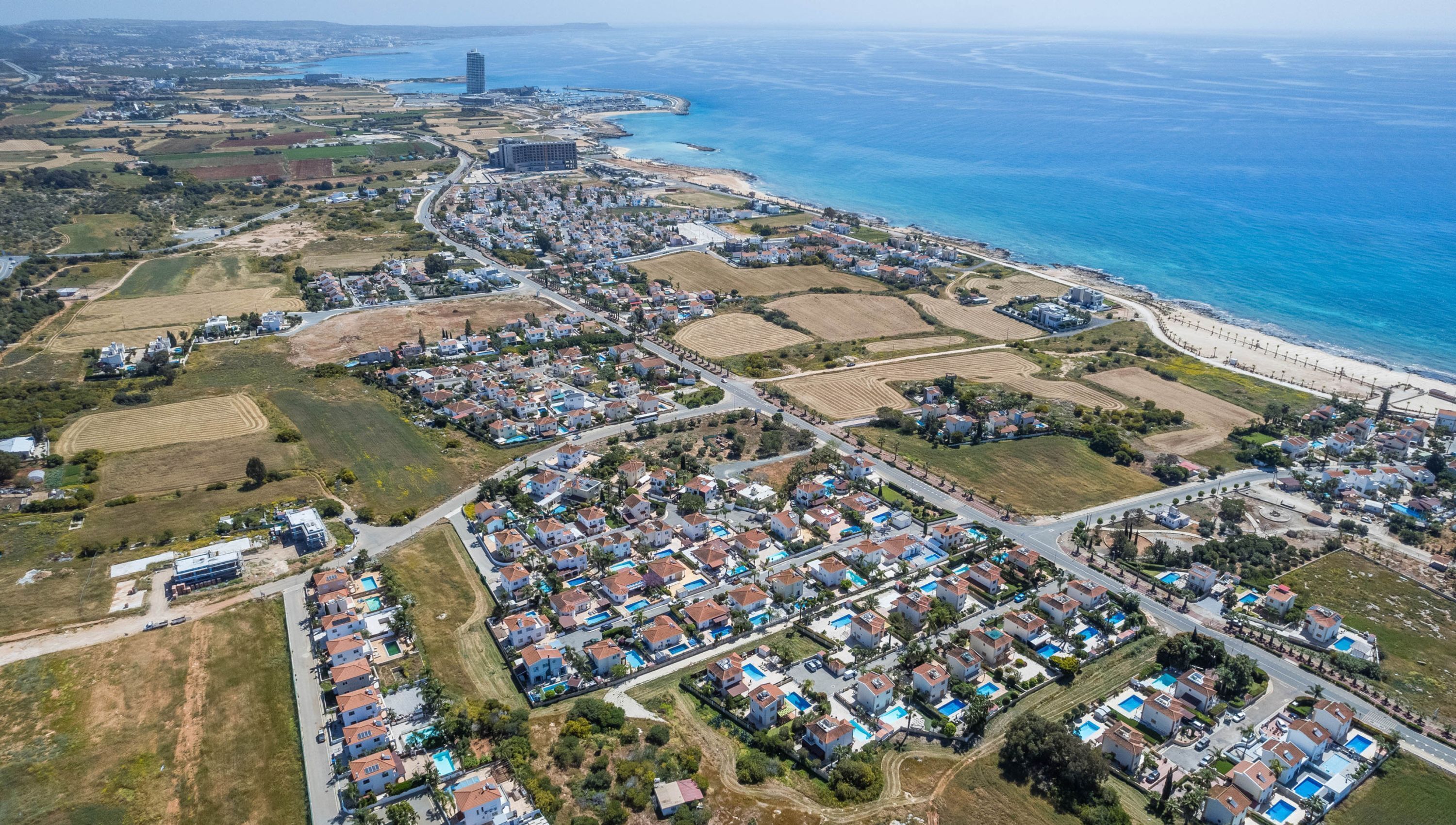 An aerial view of a coastal residential area with houses, fields, and a beach.