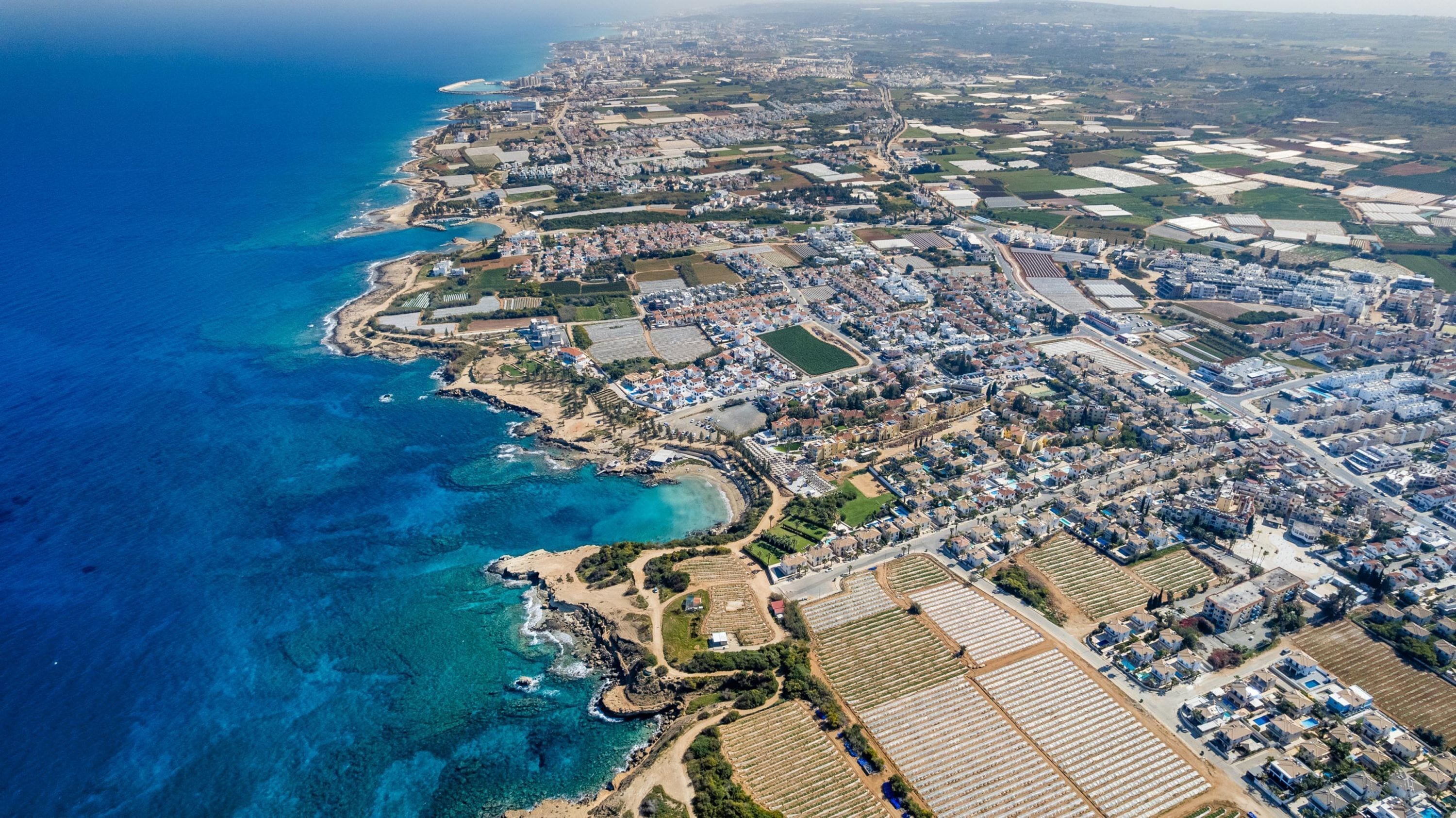 An aerial view of a coastal town with residential areas, agricultural fields, and a coastline.
