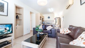 A modern living room with a sofa, coffee table, and television. There is a kitchen area in the background. - Mythical Sands Ba09 in Protaras (Paralimni)