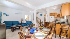A spacious living area with a blue sofa, dining table set for a meal, and a kitchen with wooden cabinets and a white refrigerator. - Villa Kos 7 in Paralimni (Paralimni)