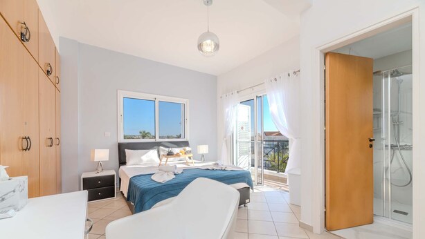 A bedroom with a bed, a bedside table, a nightstand, a bathroom with a shower, and a balcony with a view. - Nemea Serenity Blue in Ayia Napa (Ayia Napa)