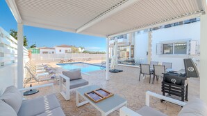 A covered outdoor area with a pool, lounge chairs, a barbecue grill, and a dining setup. - Nemea Serenity Blue in Ayia Napa (Ayia Napa)
