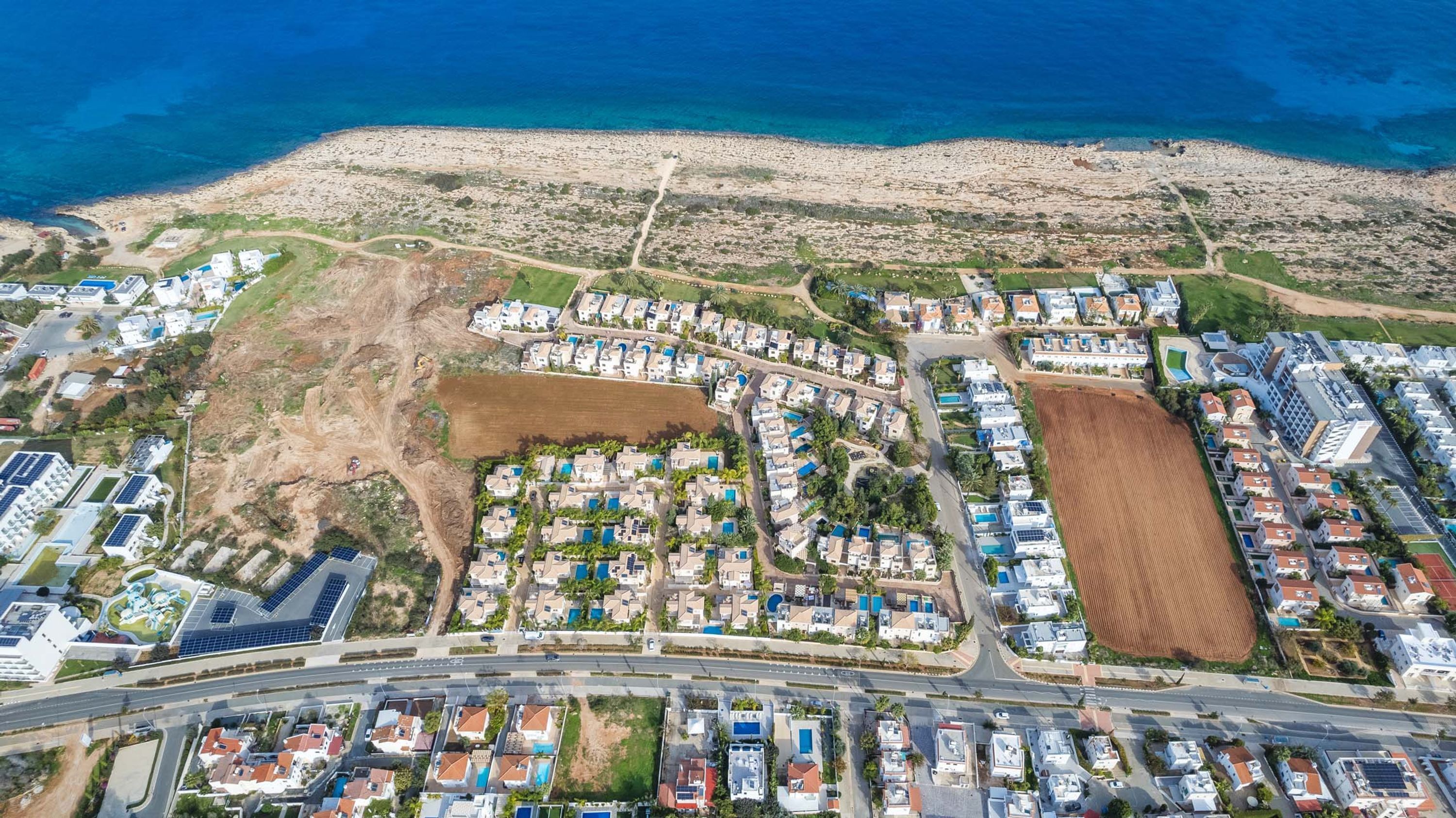 Vue aérienne d’une zone résidentielle côtière comprenant plusieurs complexes d’habitation, une route principale et une plage en arrière-plan.
