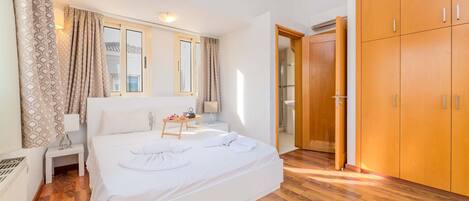 A bedroom with a large bed, wooden flooring, a wardrobe, and a window with curtains.