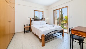 A bedroom with a bed, a wooden table, and a chair. - Villa Stephanie Oasis (Sotira)
