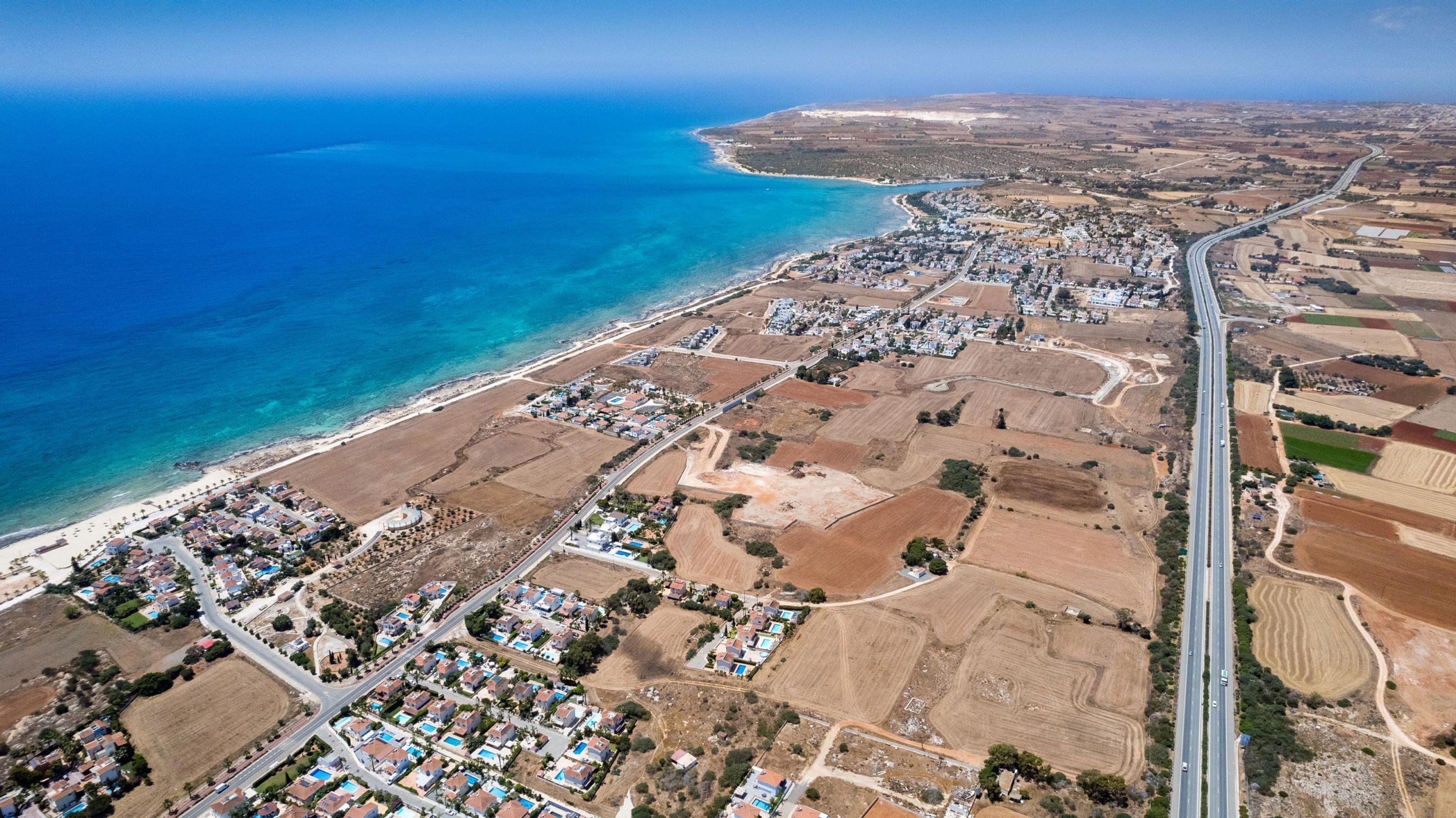 An aerial view of a coastal town with residential areas, a beach, and agricultural fields.