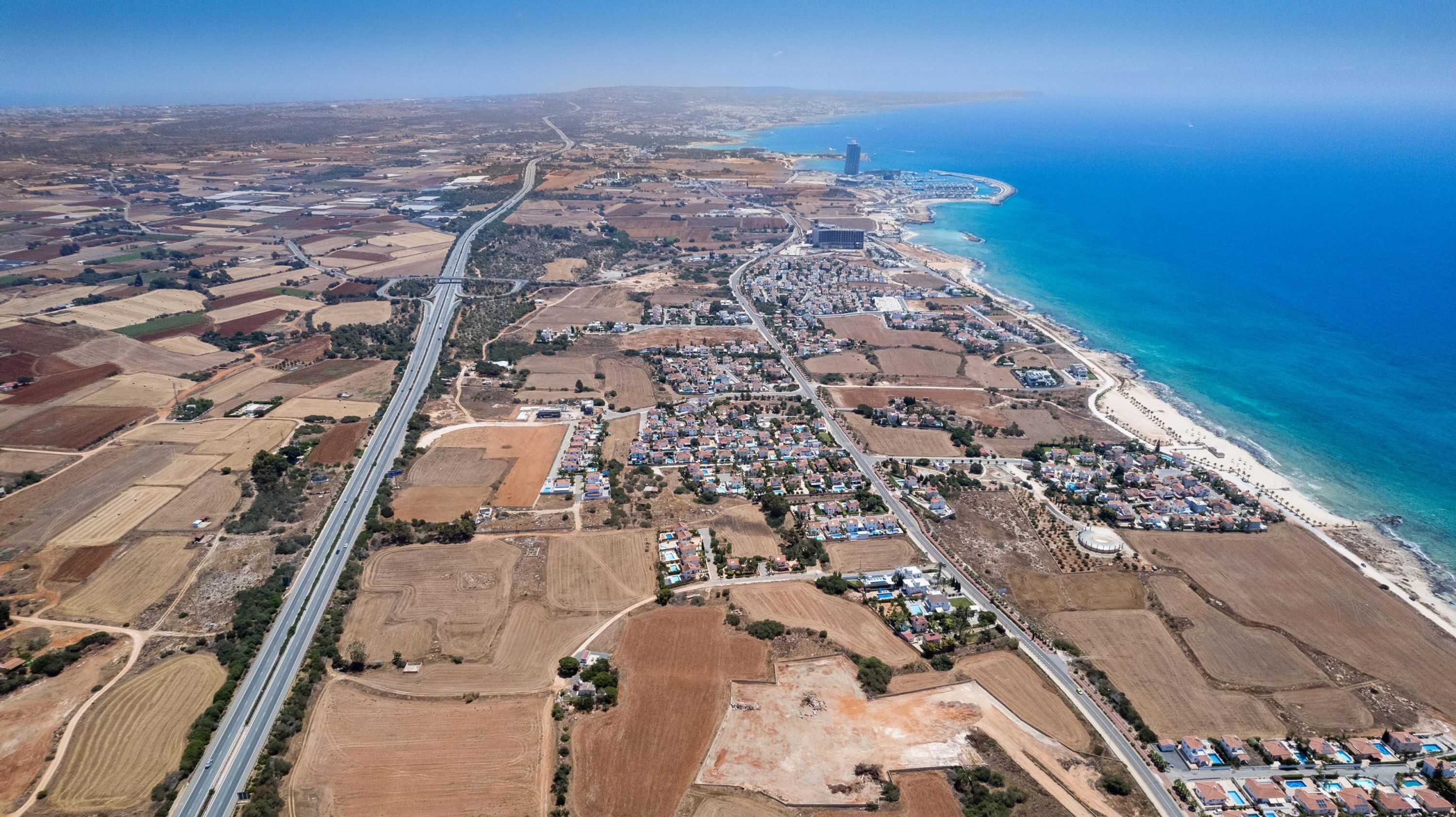 Vista aérea de uma cidade costeira, com uma estrada principal, áreas residenciais e uma praia.
