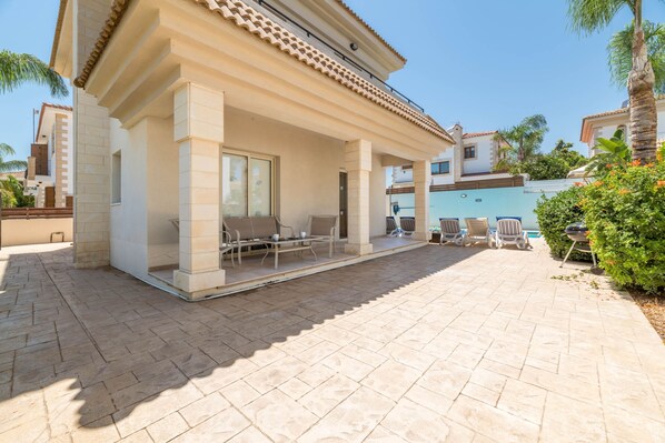 A covered outdoor area with a patio, seating, and a pool.