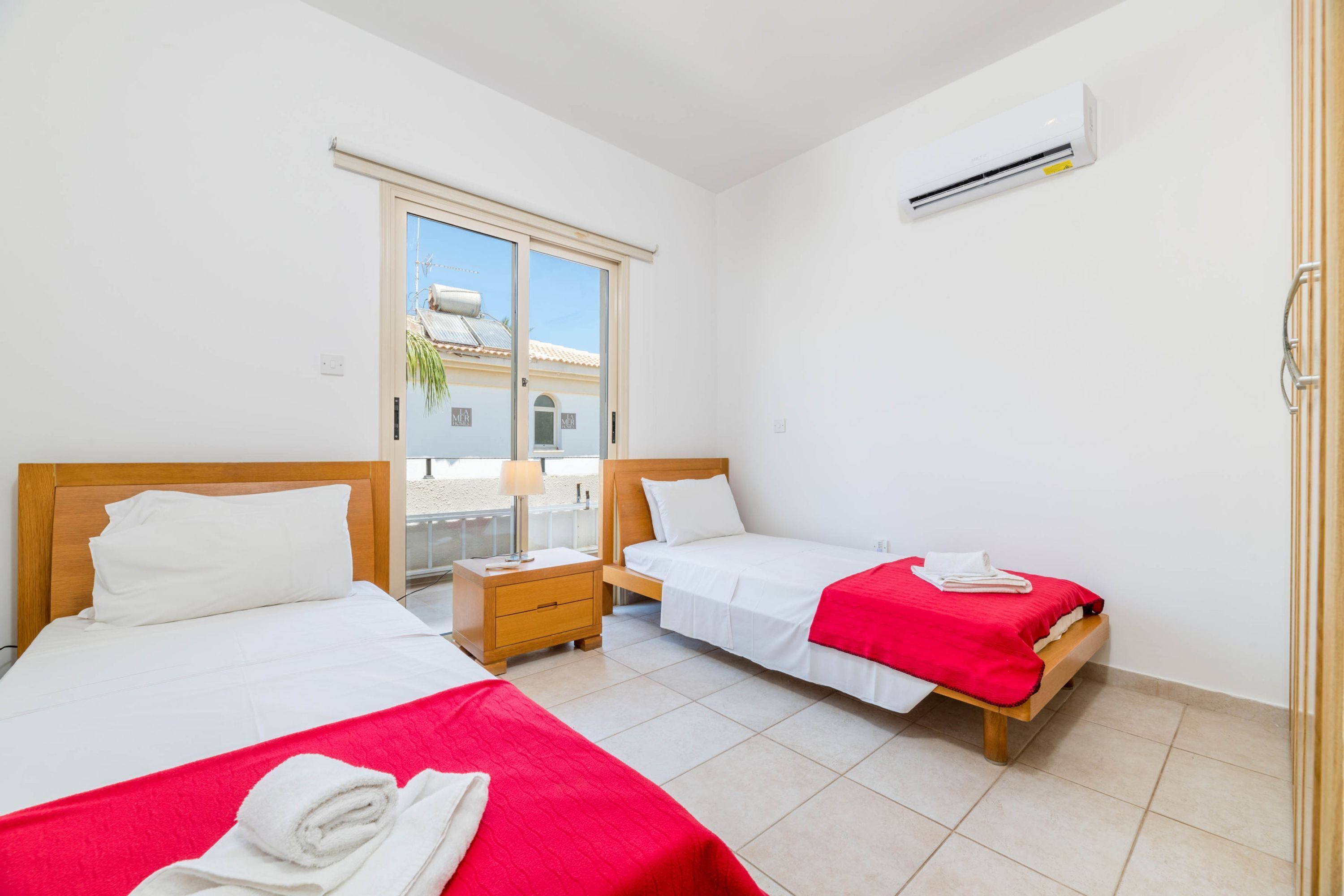 Een hotelkamer met twee bedden, een schuifdeur naar het balkon en een airconditioning op de muur.
