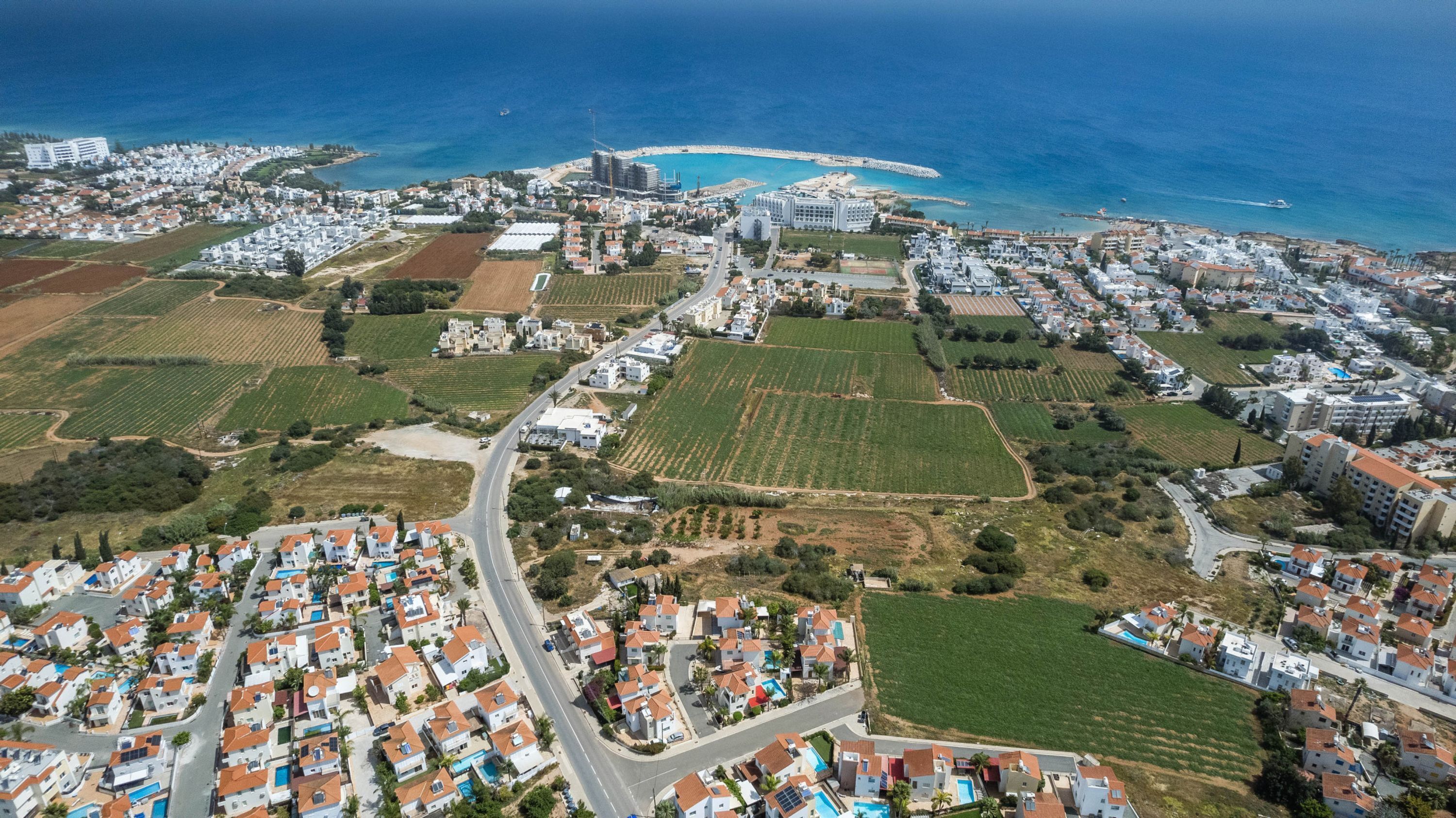 An aerial view of a coastal town with residential areas, agricultural fields, and a marina.