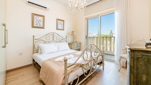 Un dormitorio con cama, cómoda, mesita de noche, candelabro y balcón con vistas.