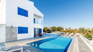 Un edificio moderno de dos pisos con piscina, mobiliario exterior y una vista despejada del paisaje circundante.