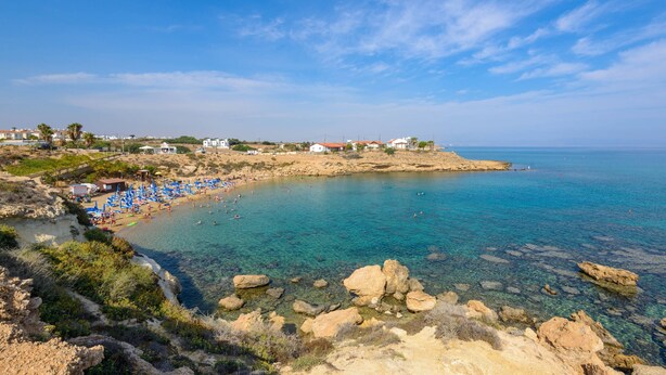 Una playa costera con aguas cristalinas, costa rocosa y sombrillas.