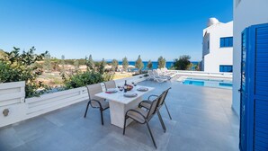 Un patio exterior con una mesa lista para comer, con vistas a una piscina y un cielo azul despejado.