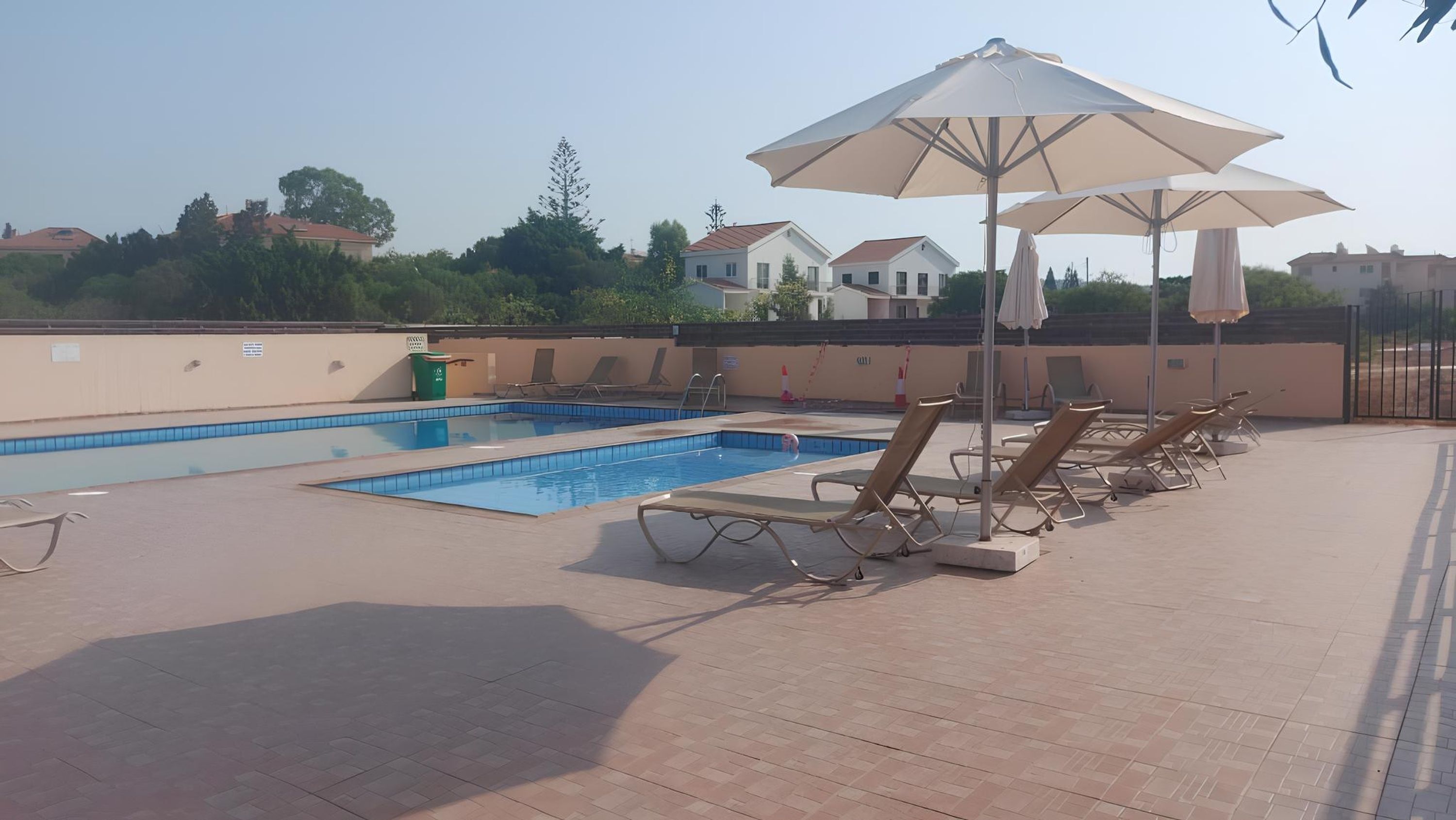 Una piscina con lettini e ombrelloni, circondata da un solarium piastrellato e un muretto.